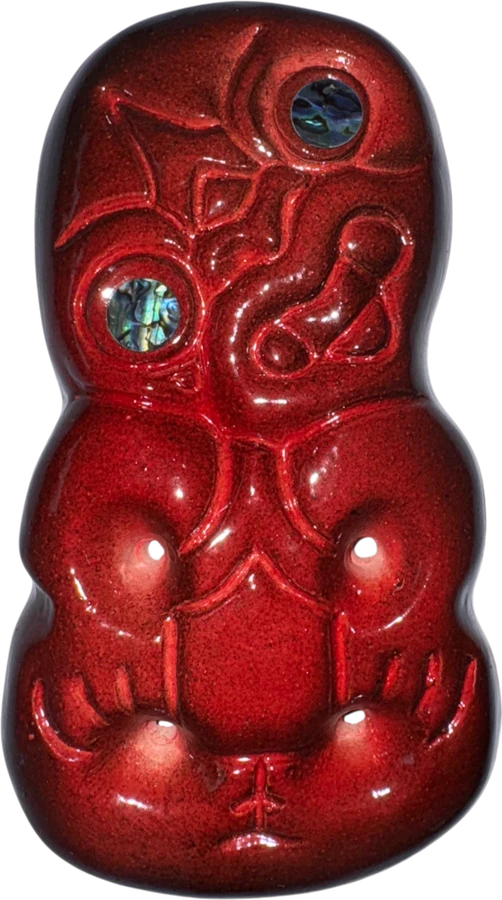 Red-glazed ceramic hei tiki with paua shell set into its eyes
