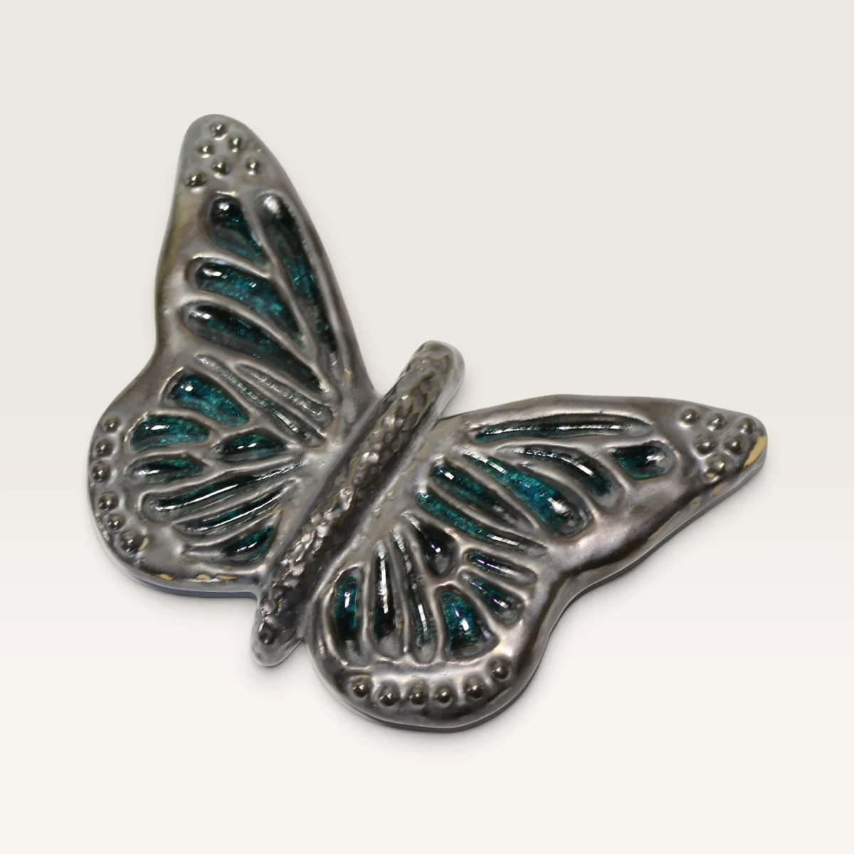Ceramic butterfly with a silvery pewter-look finish and teal glass inlaid between the raised veins of its wings