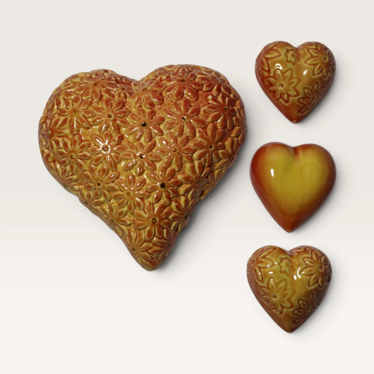 Orange-gold ceramic heart covered in pressed flowers, beside three small matching hearts
