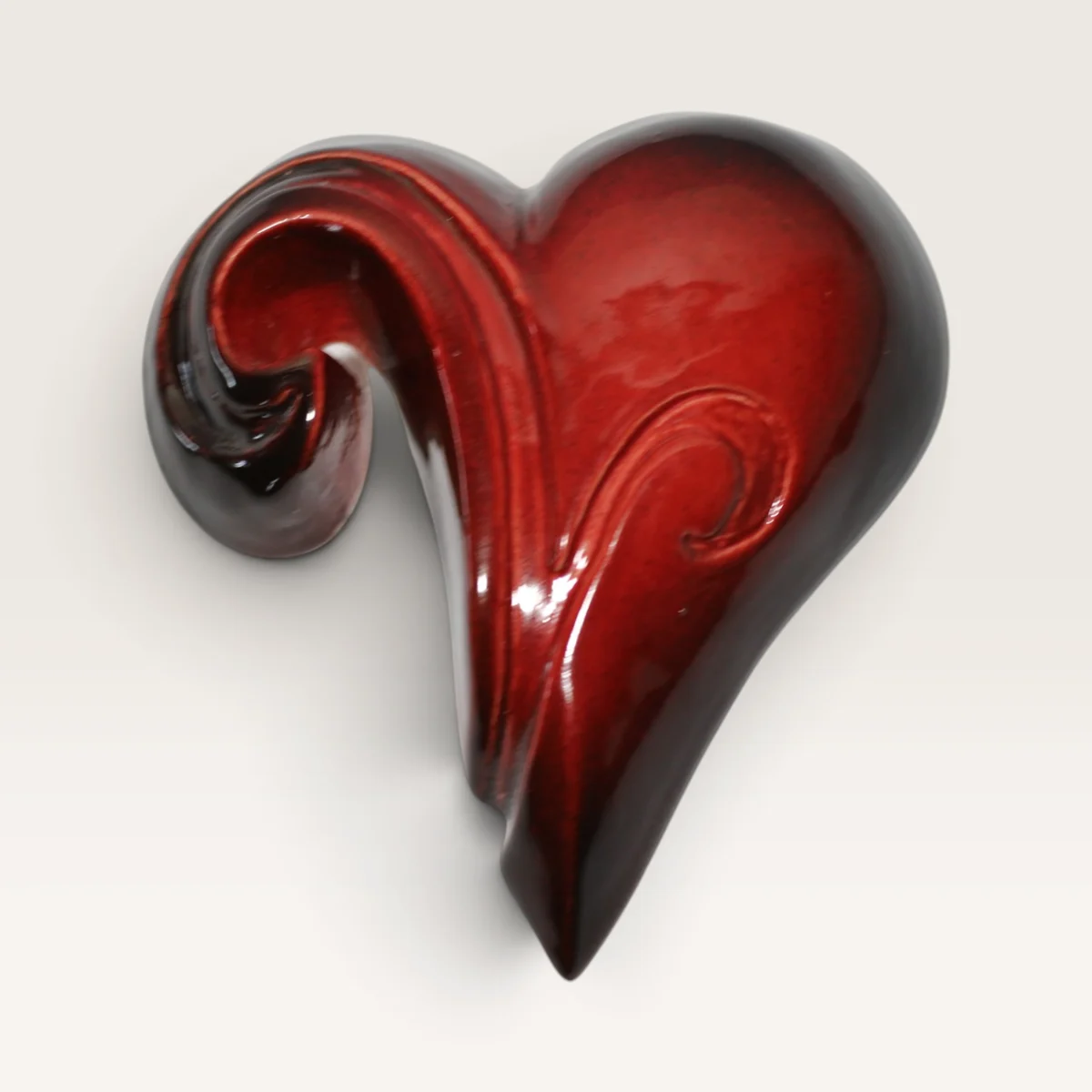 Glossy red ceramic heart whose top curls over into a koru spiral, darkening to near-black at the edges
