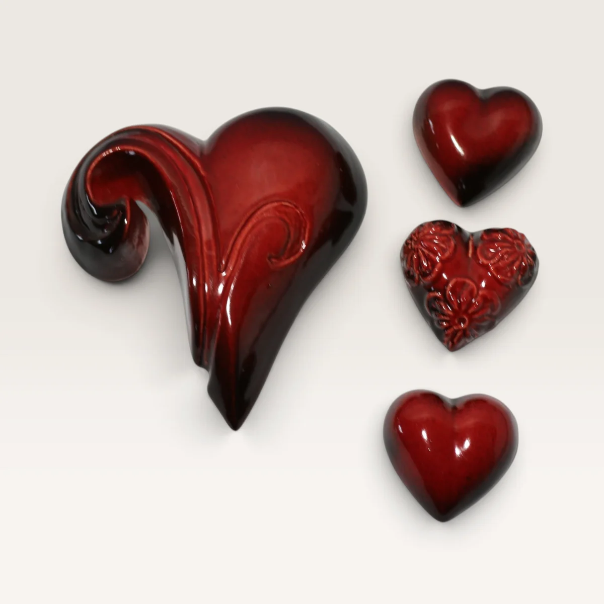 Red ceramic koru heart beside three small red hearts, one of them pressed with flowers