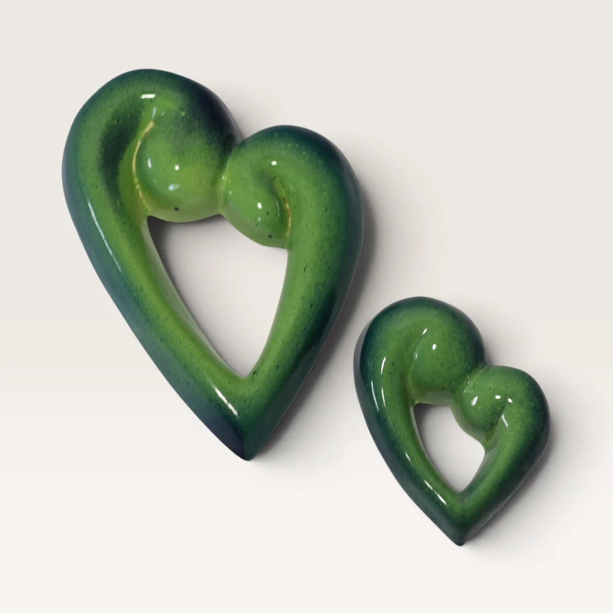 Two open green ceramic koru hearts, one large and one small, darkening to blue-green at the edges