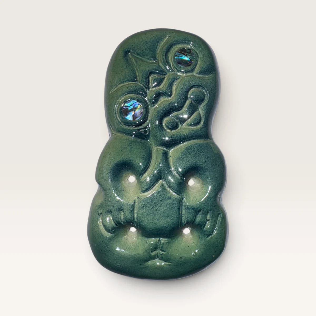 Sage-green ceramic hei tiki with paua shell set into its eyes