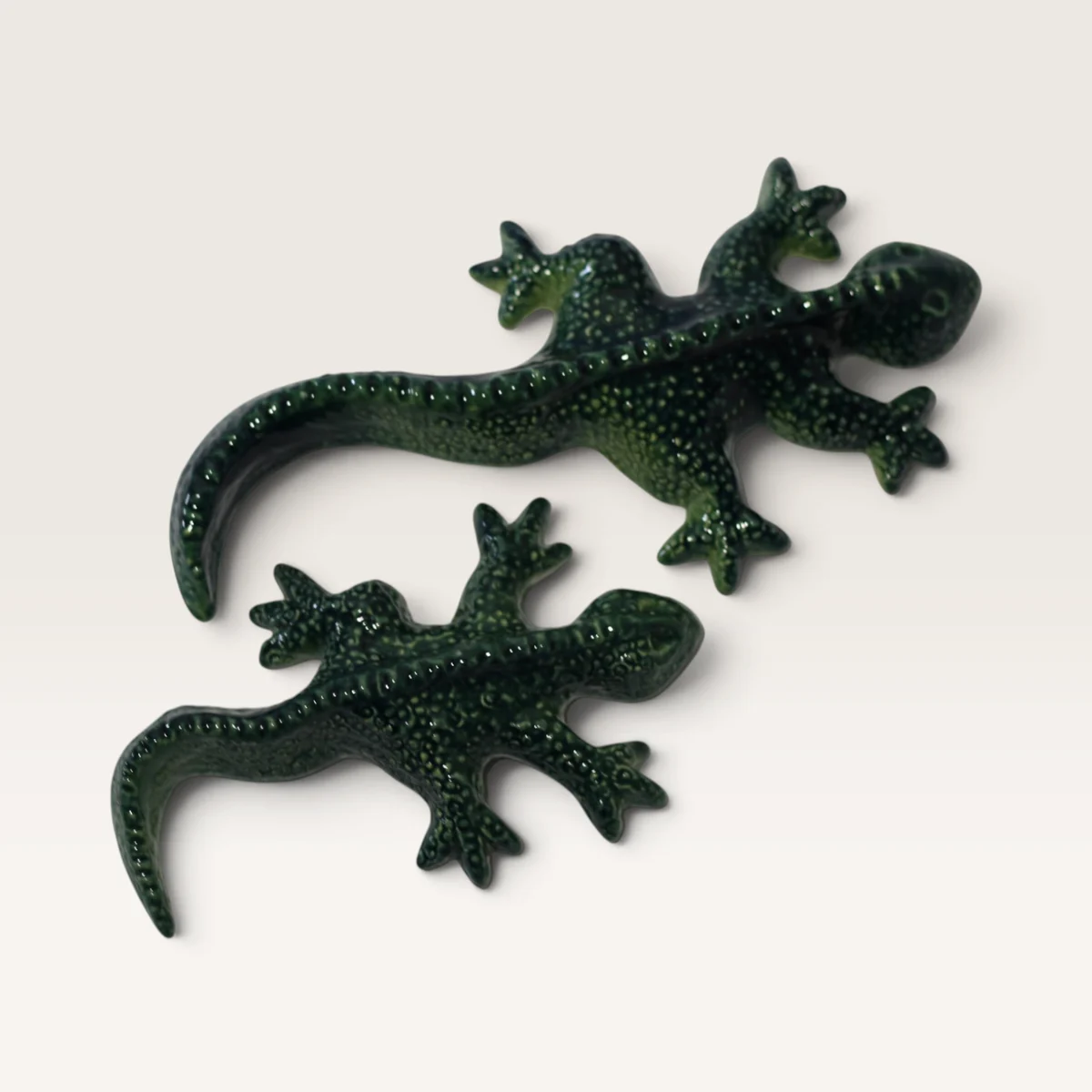 Two speckled dark green ceramic geckos, one larger than the other