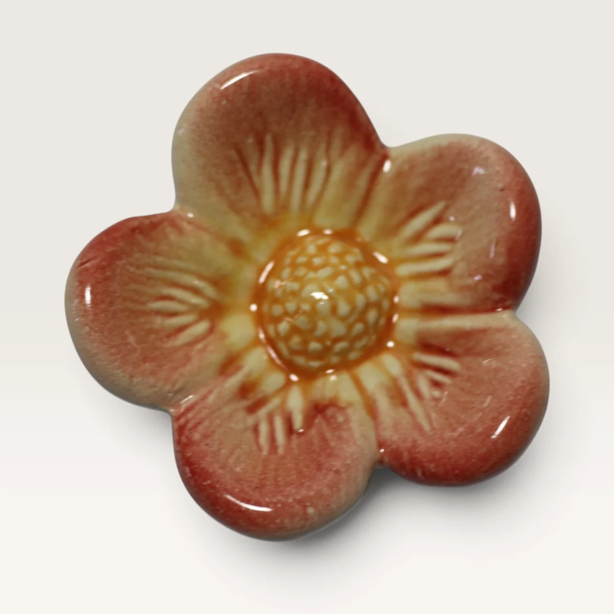 Small five-petal ceramic flower in dusty red fading to yellow, with a textured yellow centre