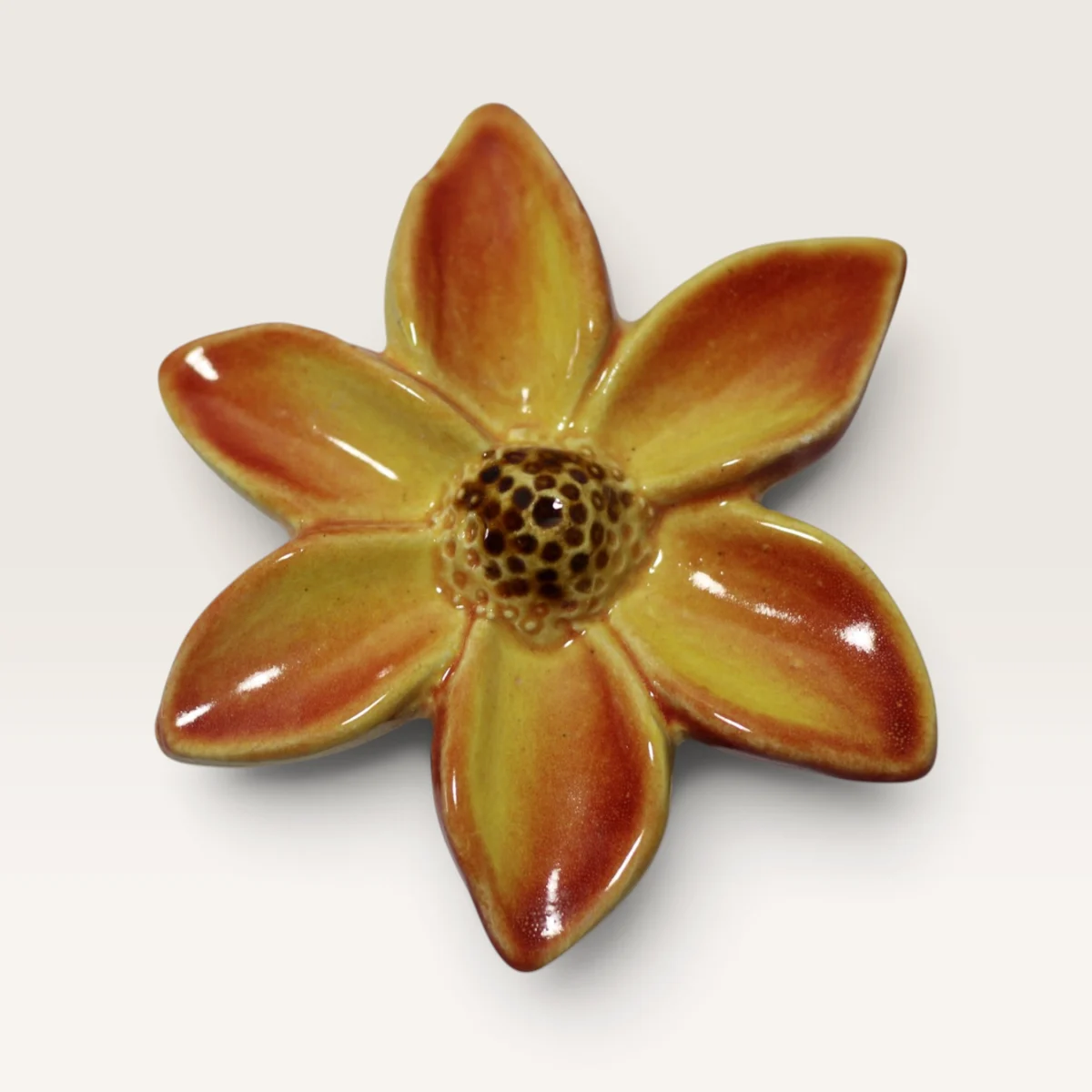 Small ceramic flower with six pointed petals in orange and yellow and a speckled brown centre