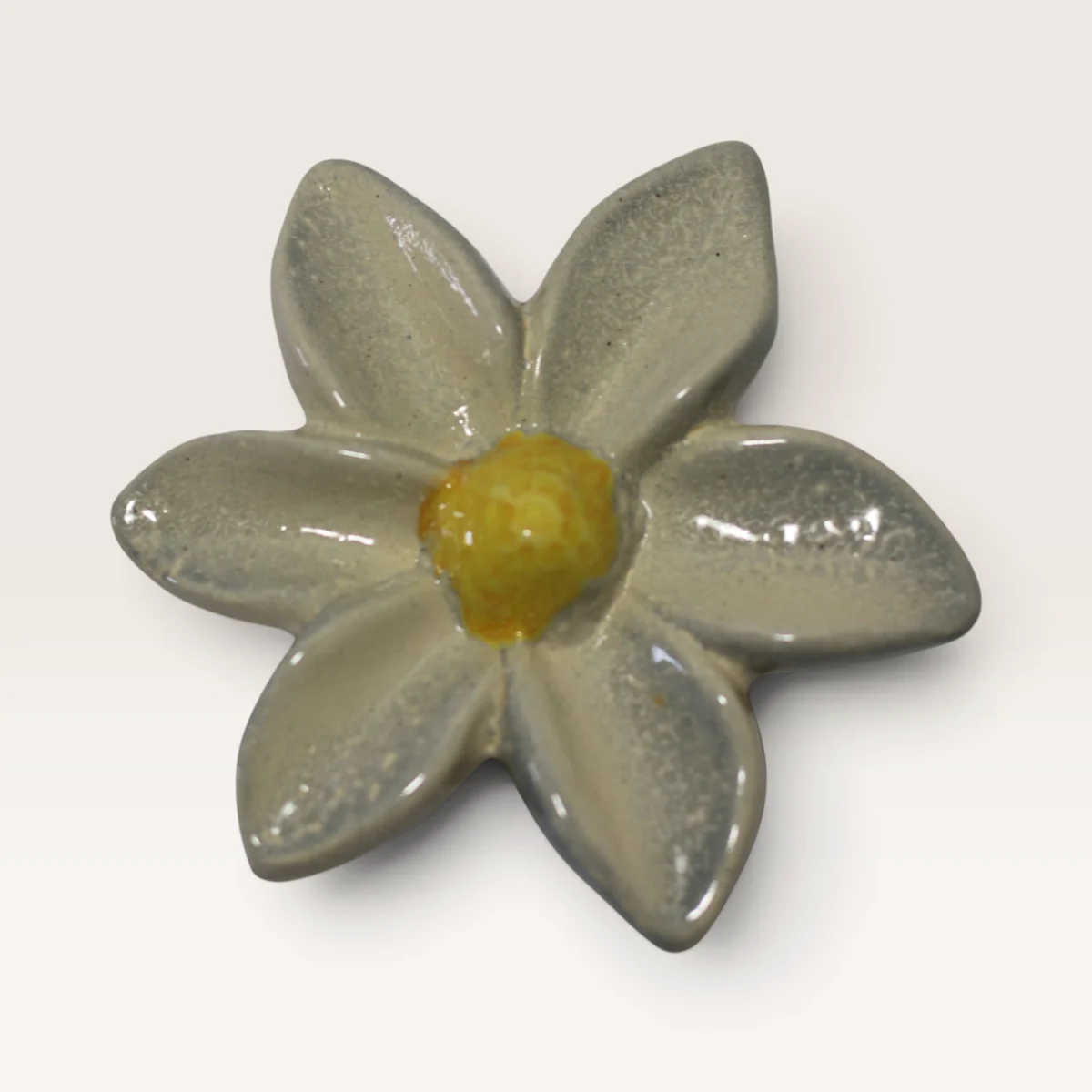 White ceramic flower with six pointed petals and a yellow centre
